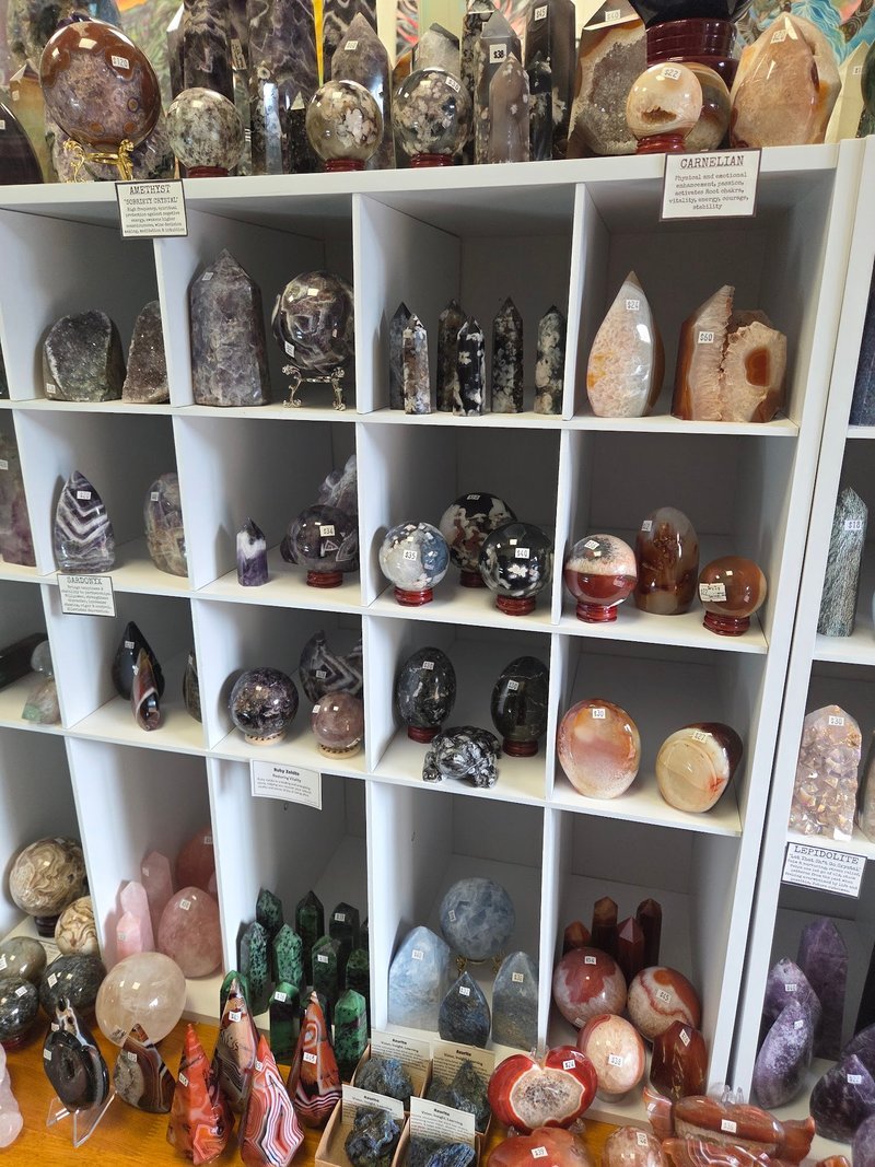 White cube shelving with polished crystal specimens including amethyst points, rose quartz towers, jasper, and agate spheres