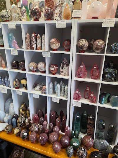 White cube shelving displaying polished crystal towers, spheres, and carved specimens including ruby, malachite, and agate