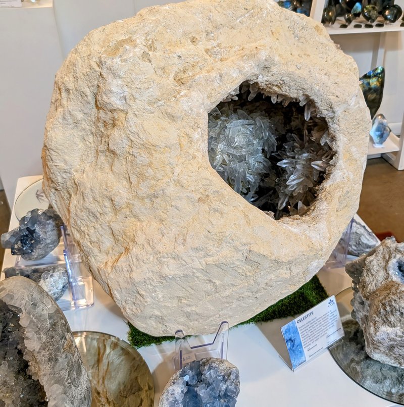 Modern gallery display with tiered white shelving showcasing polished stones, crystal points, and spheres