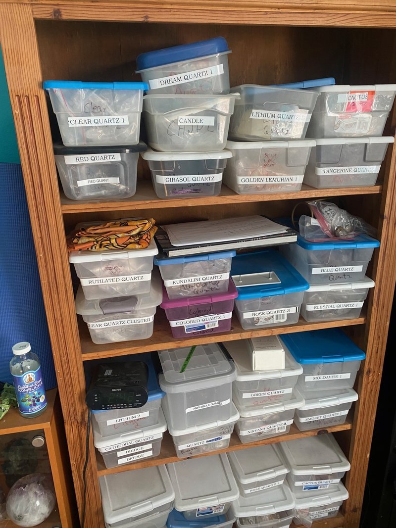Organized storage shelves with labeled plastic bins containing various quartz specimens by type