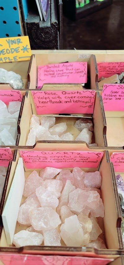 Wooden compartment bins with raw crystal specimens including banded agate, rose quartz, and clear quartz with pink labels