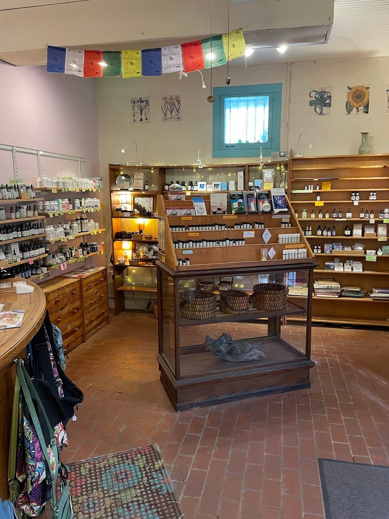 Apothecary interior with Tibetan prayer flags, wooden shelving displaying herbal products and metaphysical supplies
